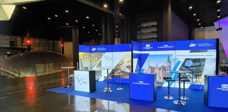 Strefy wystawców z podświetlanymi ladami i grafiką z projektami infrastruktury