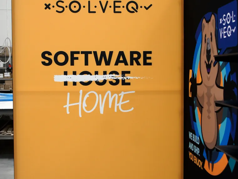 Pomarańczowa ściana z logo Solveq i hasłem Software House Home z przekreślonym słowem House